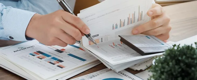 Person analyzing financial charts and reports with calculator and documents on desk.